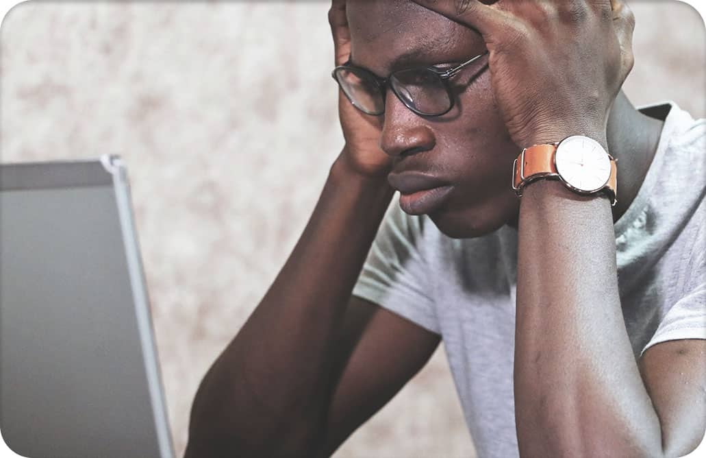 man staring at laptop screen, holding head in hands