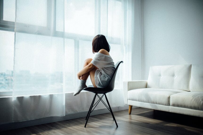 Woman sitting in an airy room in comfortable clothing looking out the window. Hosted by Wellin5