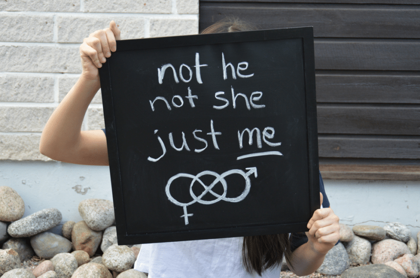 A nonbinary person holds up a sign reading “Not he, not she, just me.”