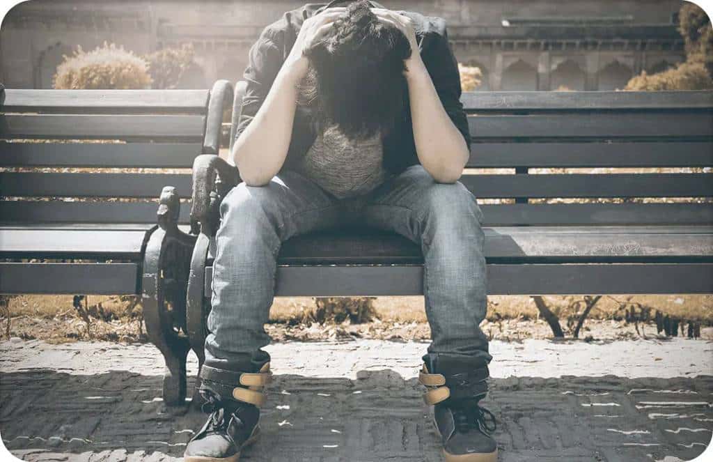 Man holding head in arms on bench