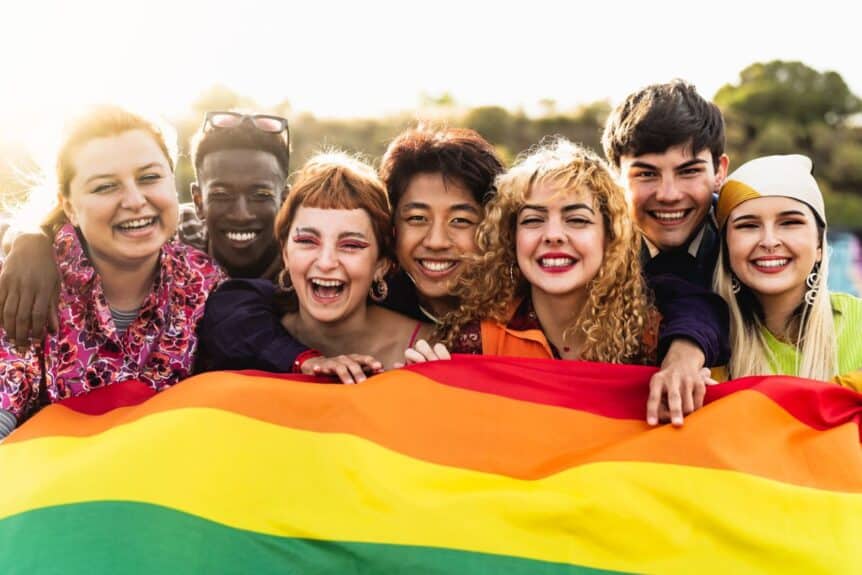 A diverse group of friends hold up a pride flag.