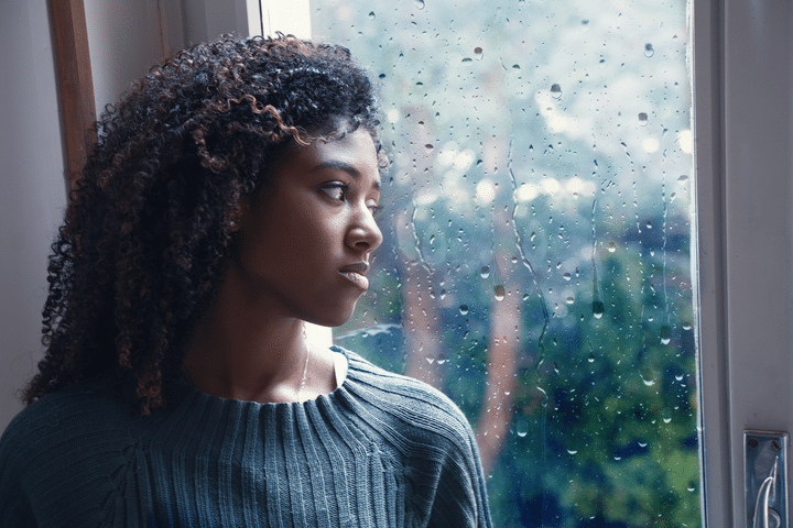 A woman looks pensively out of a rain-streaked window.